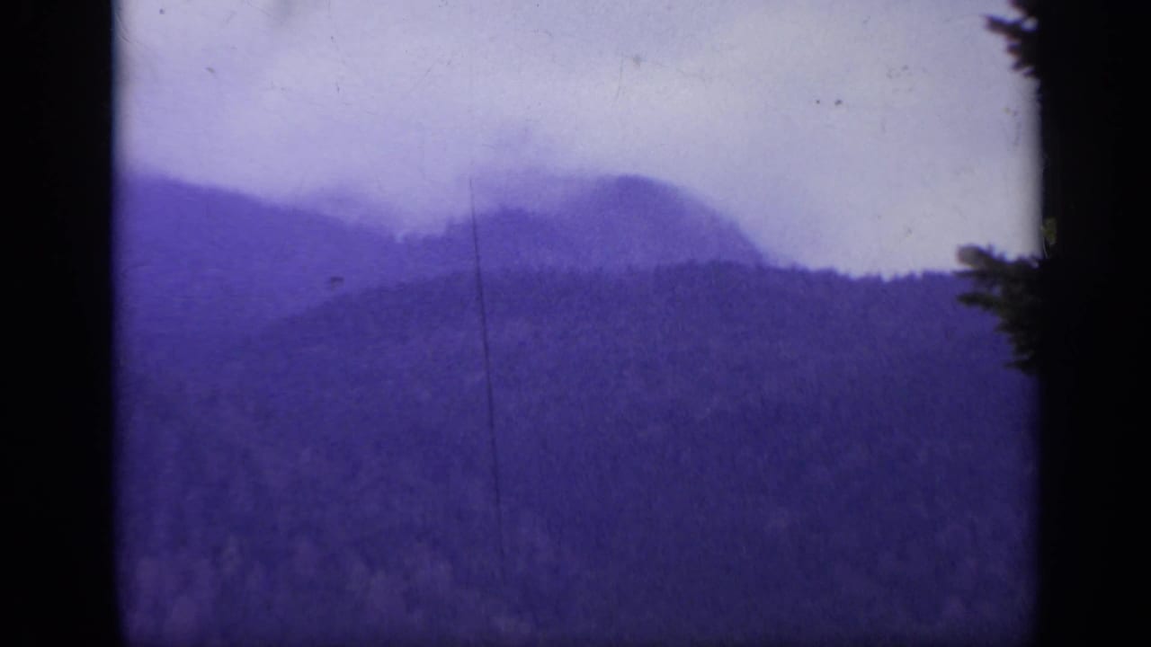 Layered wooded hills and a pale sky with dark film borders and a vertical scratch.
