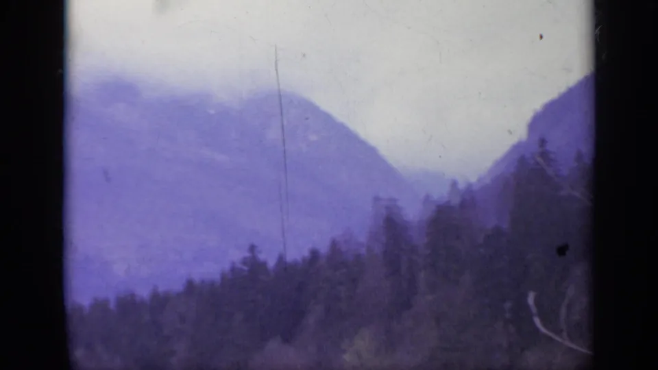 1962 Italy 8mm view of a foggy mountain ridge rising beyond a dark forest, with soft exposure and visible film gate edges.