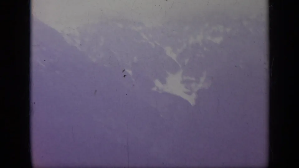 1962 Italy home-movie frame showing a hazy mountain slope with patches of snow, softened by exposure and film color shift.