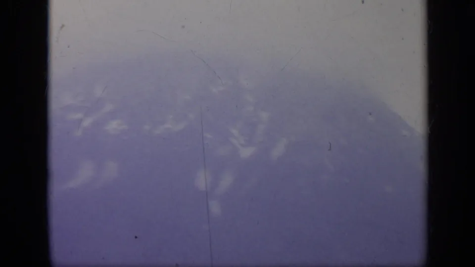 Misty Italian mountain view from the 1962 home movie, with haze, hillside vegetation, and heavy film gate borders.