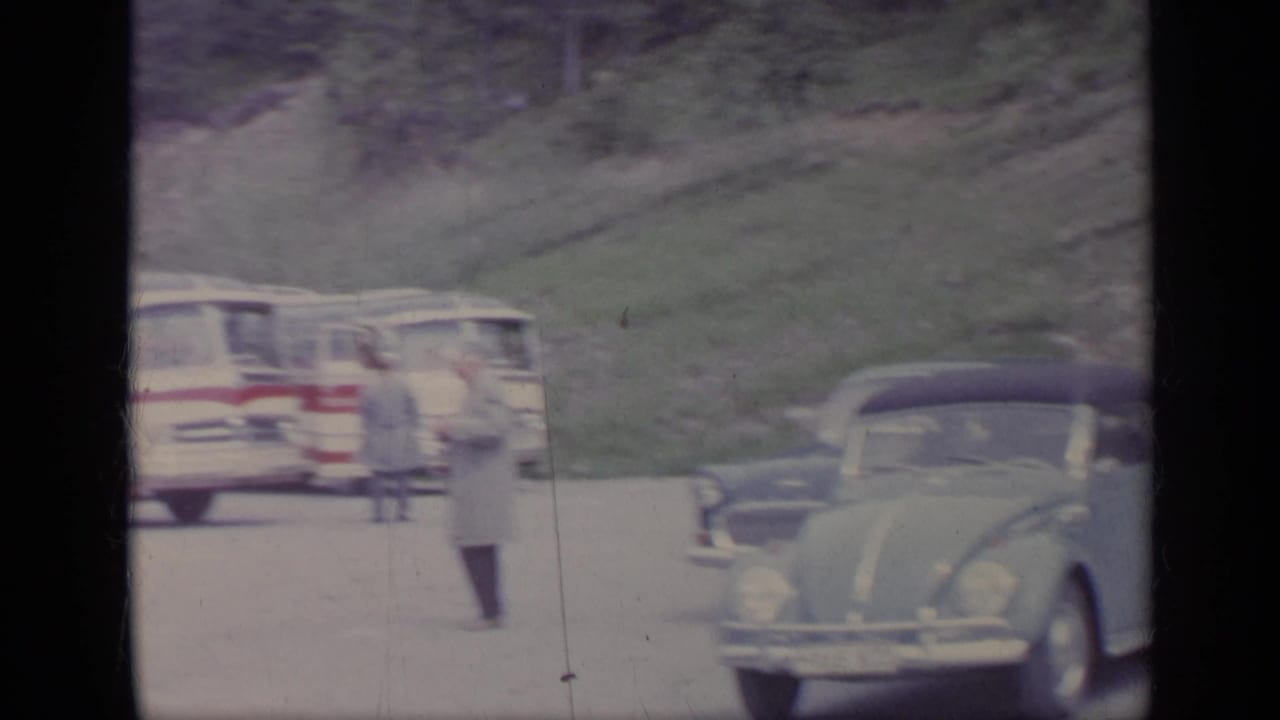 Tour bus and parked compact car beside a mountain road with a pedestrian nearby.