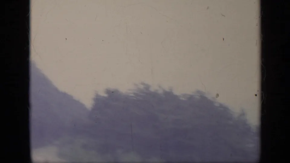 1962 Italian 8mm frame showing a hazy wooded slope or ridge, faded color, scratches, and contact-sheet borders.