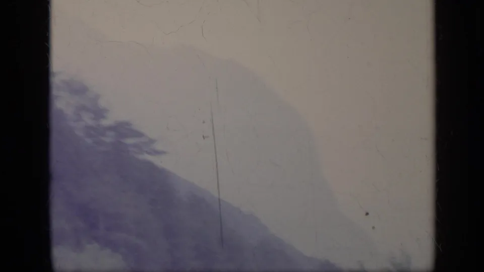 1962 Italian 8mm frame with a blurred hillside, faint tree line, pale sky, and visible aged-film dust and scratches.