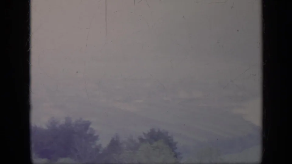 1962 Italian mountain scenery appears beyond a central dark window frame, with soft hills and trees under a muted sky.