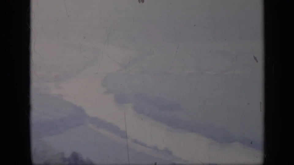 A soft 1962 Italy 8mm view shows a pale winding valley or river below distant slopes, partly blocked by dark window framing.