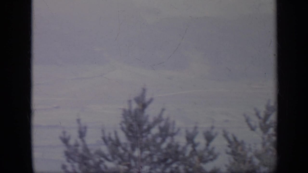 1962 Italy 8mm frame showing a hazy mountain valley through a dark window frame, with evergreen silhouettes along the lower edge.