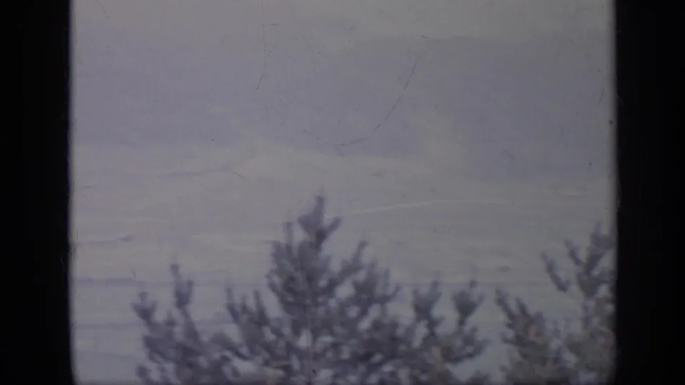 1962 Italy 8mm frame showing a hazy mountain valley through a dark window frame, with evergreen silhouettes along the lower edge.