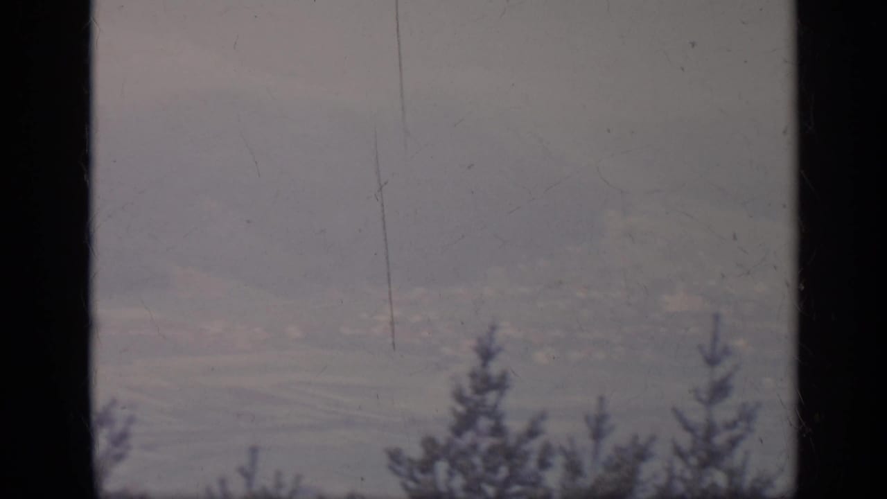 Hazy mountain landscape with evergreen silhouettes and a dark vertical window bar.