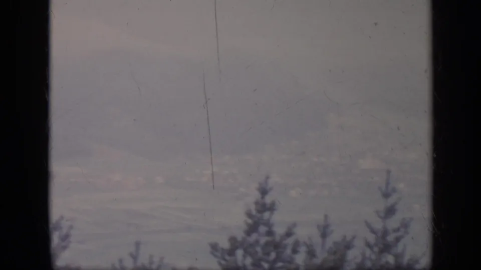 1962 Italy 8mm view of a misty mountain valley, partly divided by a dark window bar, with soft tree silhouettes in the foreground.