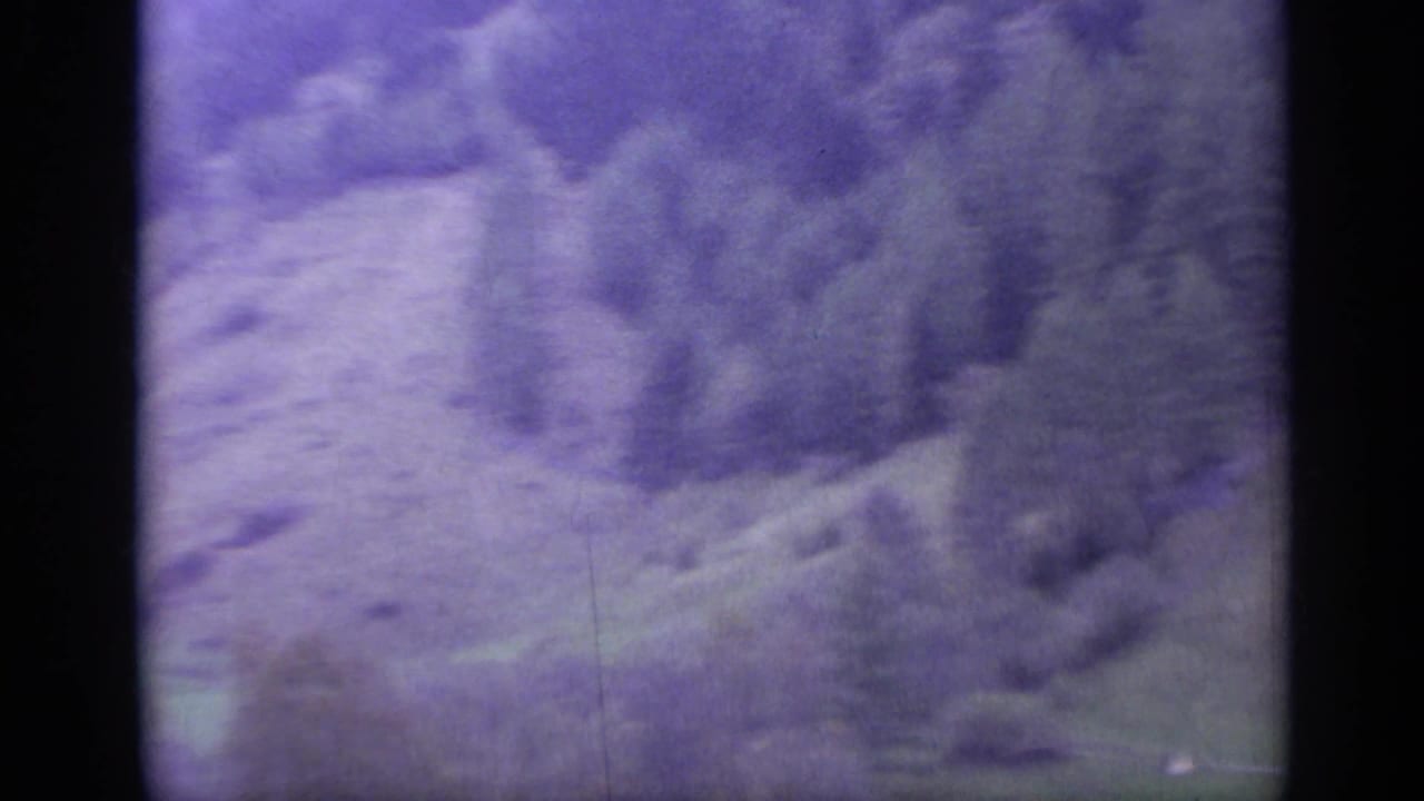 1962 Italy 8mm frame with purple-blue cast over rugged mountain terrain, soft focus, visible grain, and dark frame borders.
