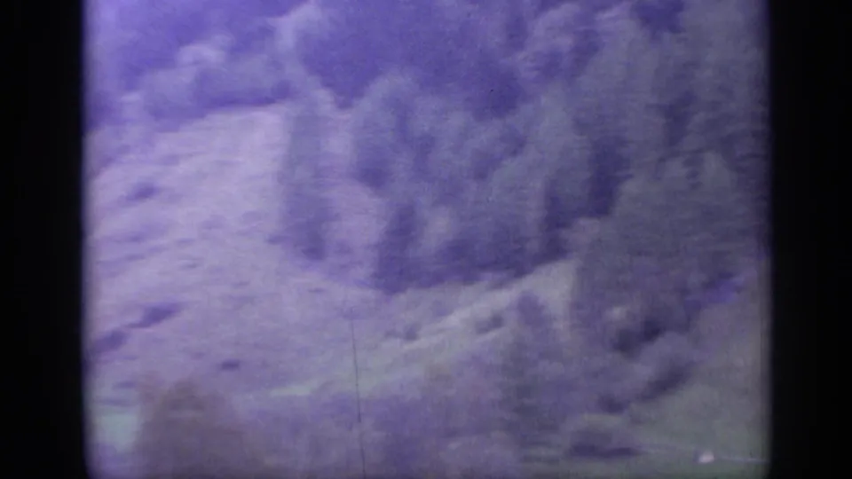 1962 Italy 8mm frame with purple-blue cast over rugged mountain terrain, soft focus, visible grain, and dark frame borders.