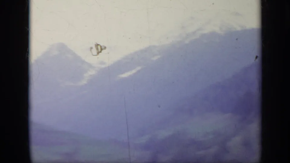 1962 Italy 8mm frame showing pale sky above snow-dusted mountain peaks and layered blue ridges with dust and scratches visible.