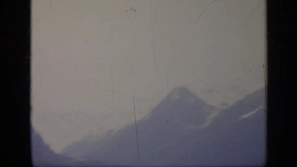 1962 Italy 8mm frame with distant blue mountain peaks low in the composition, pale sky, soft exposure, and visible film scratches.