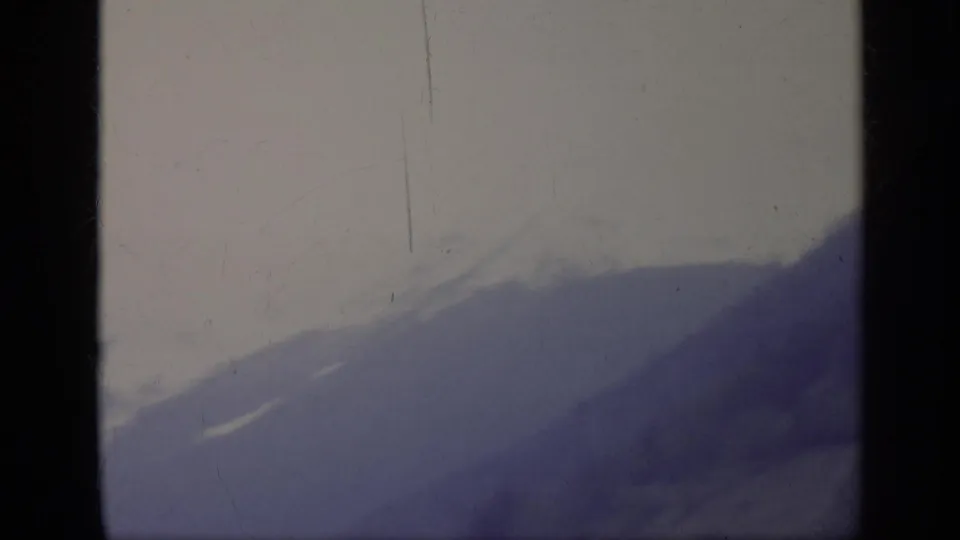 1962 8mm home-movie view in Italy of a hazy mountain slope and pale sky, framed by dark film edges.