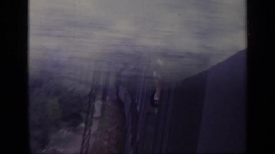 1962 Italy 8mm frame from a train-side viewpoint, with a passenger shape near the window and blurred Alpine landscape outside.