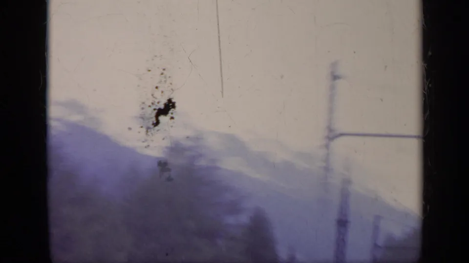 Soft 8mm frame from a 1962 Italy train journey, showing hazy alpine ridges, an overhead pole, and visible film wear.