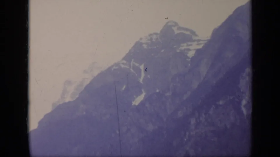 1962 Italy 8mm home-movie frame showing hazy snow-capped mountains with a strong purple cast and visible film wear.