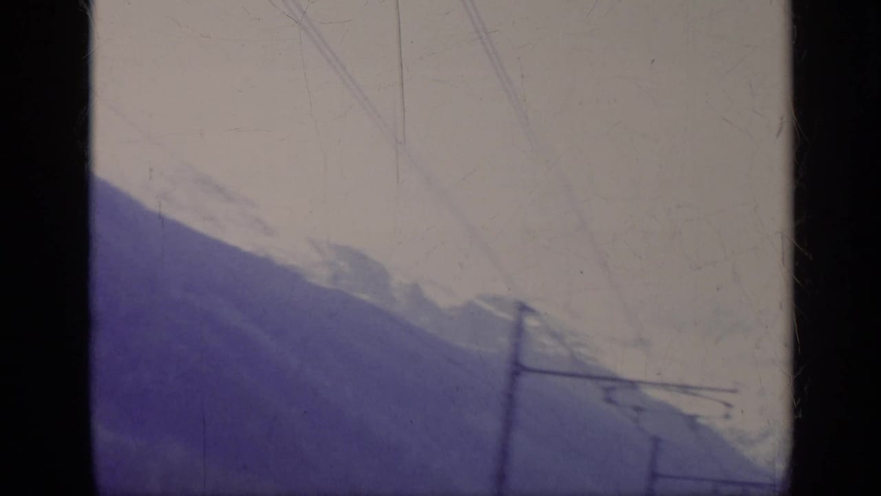 Snowy mountain range beyond a valley, seen through dark window edges with overhead lines crossing the frame.