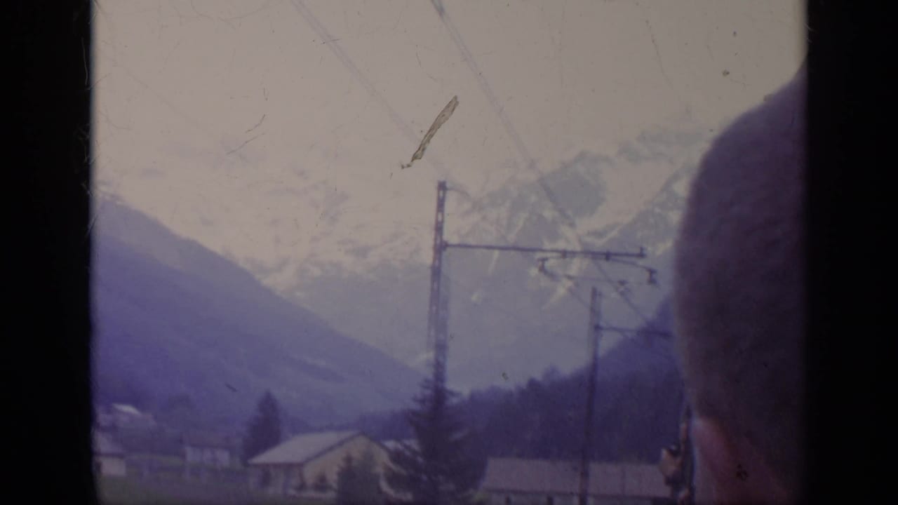 Mountain valley with utility poles, overhead wires, buildings, and a partial figure at the right edge.