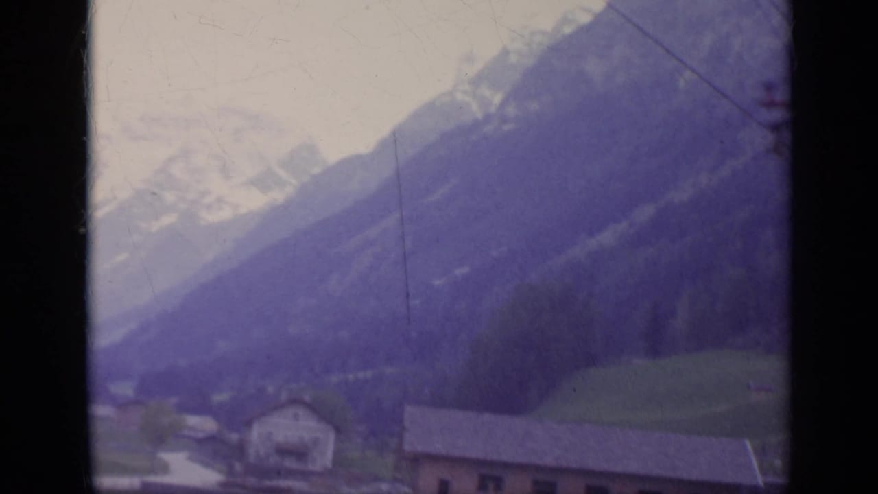 Mountain valley with houses below snow-capped peaks.