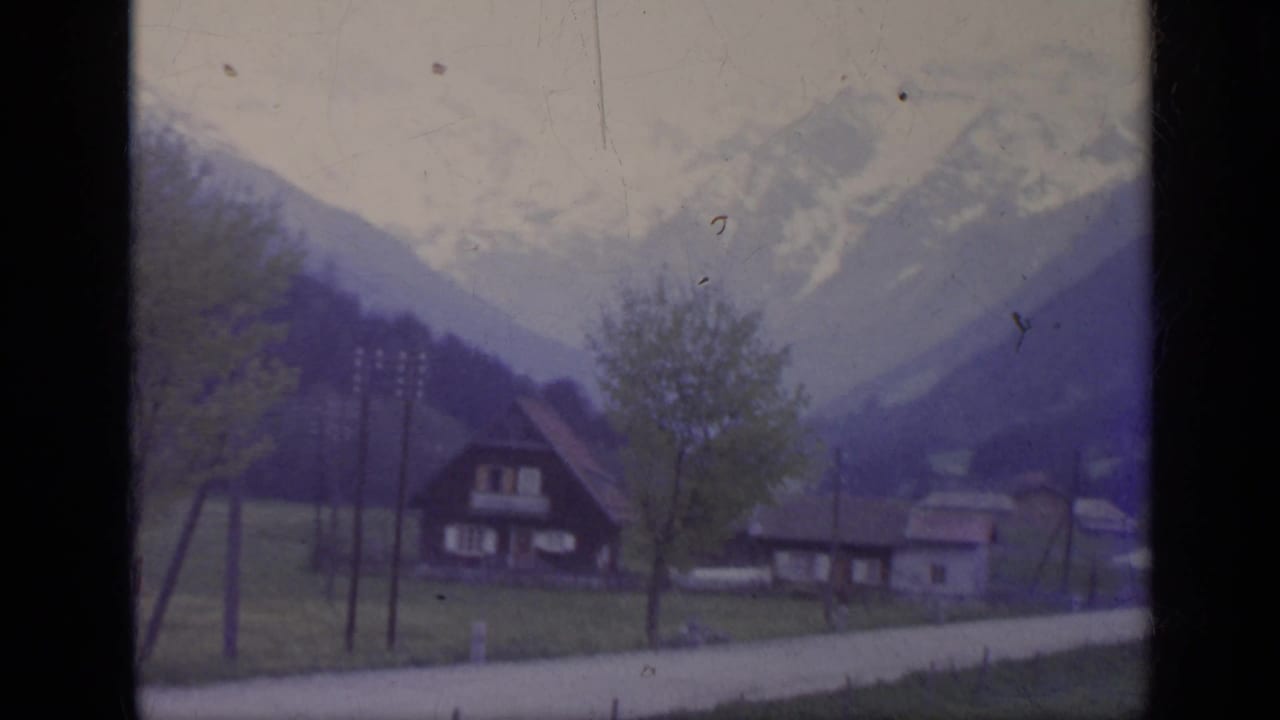 Village houses, road, trees, and mountains seen through a train window.