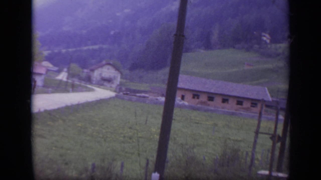 Green hillside, road, buildings, and utility pole beside the rail line.