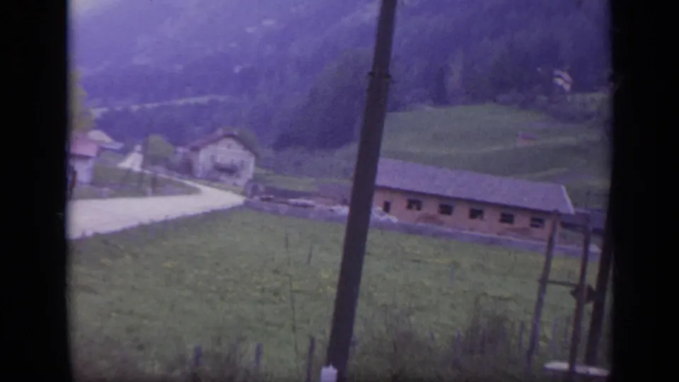Rural Italian hillside and village buildings pass the train window, with a utility pole in the foreground.
