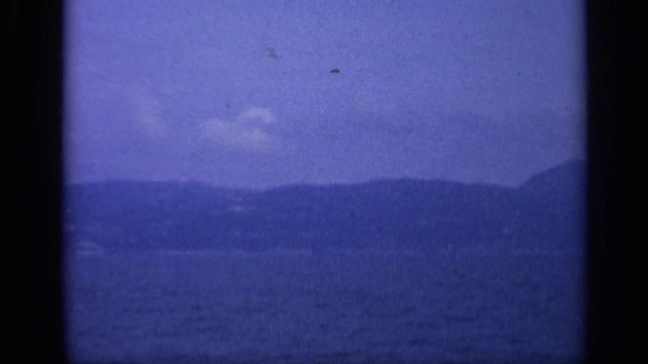 A hazy Italian coastal mountain ridge appears across blue water in a cool-toned 8mm frame.