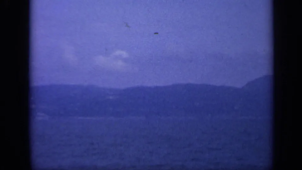 A hazy Italian coastal mountain ridge appears across blue water in a cool-toned 8mm frame.