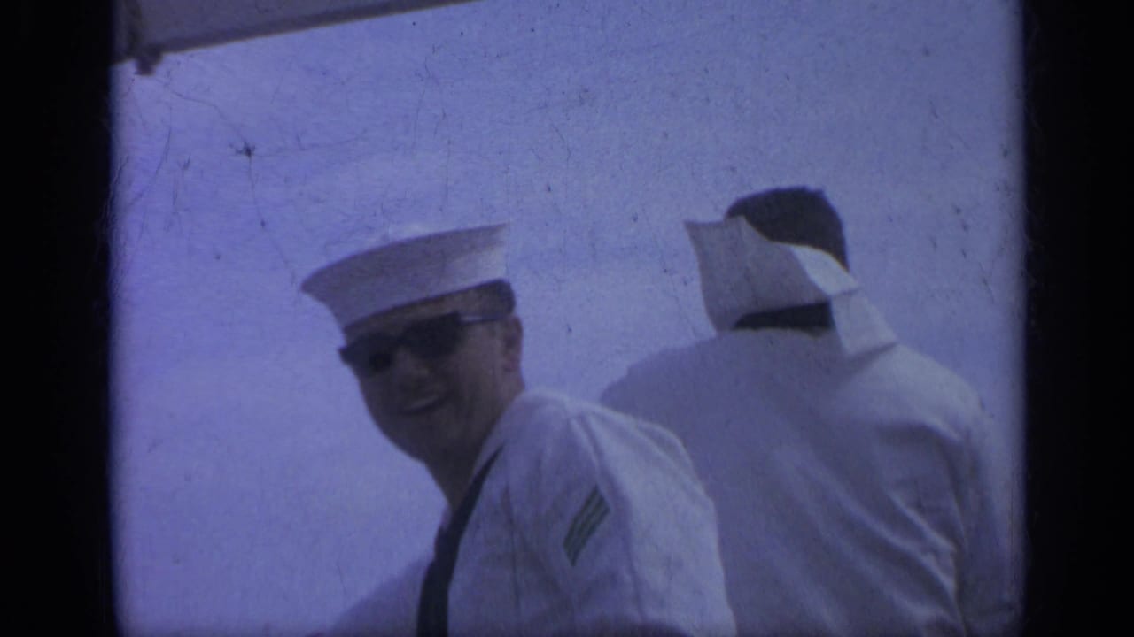 Two sailors in white uniforms aboard a ship, one smiling toward the camera.