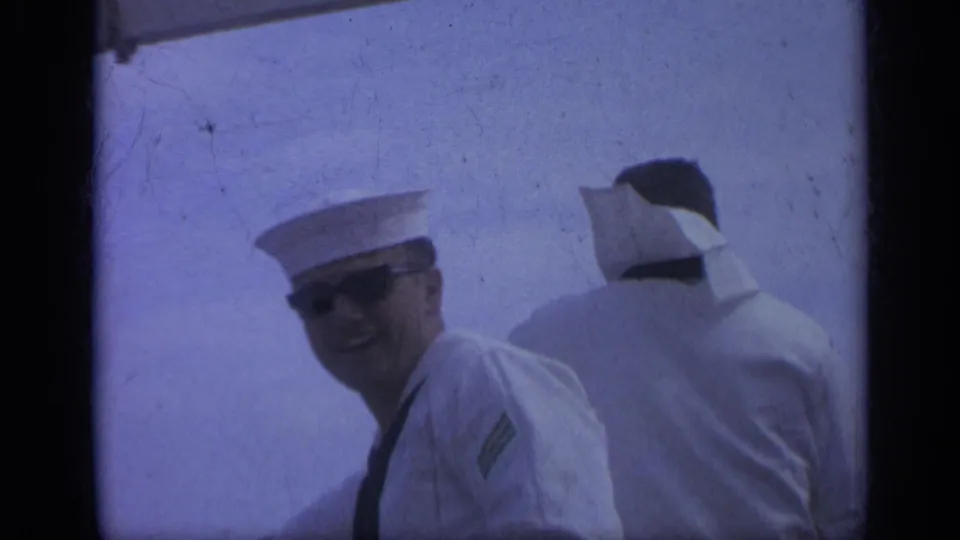 1962 Italy home-movie frame showing two sailors aboard a ship, with one in sunglasses smiling toward the camera.