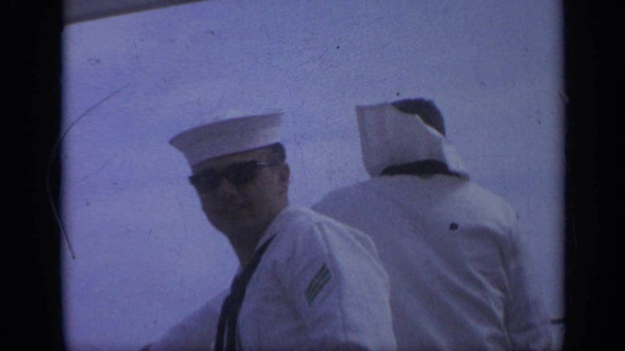 Sailor in sunglasses looks toward the camera beside another sailor facing away.