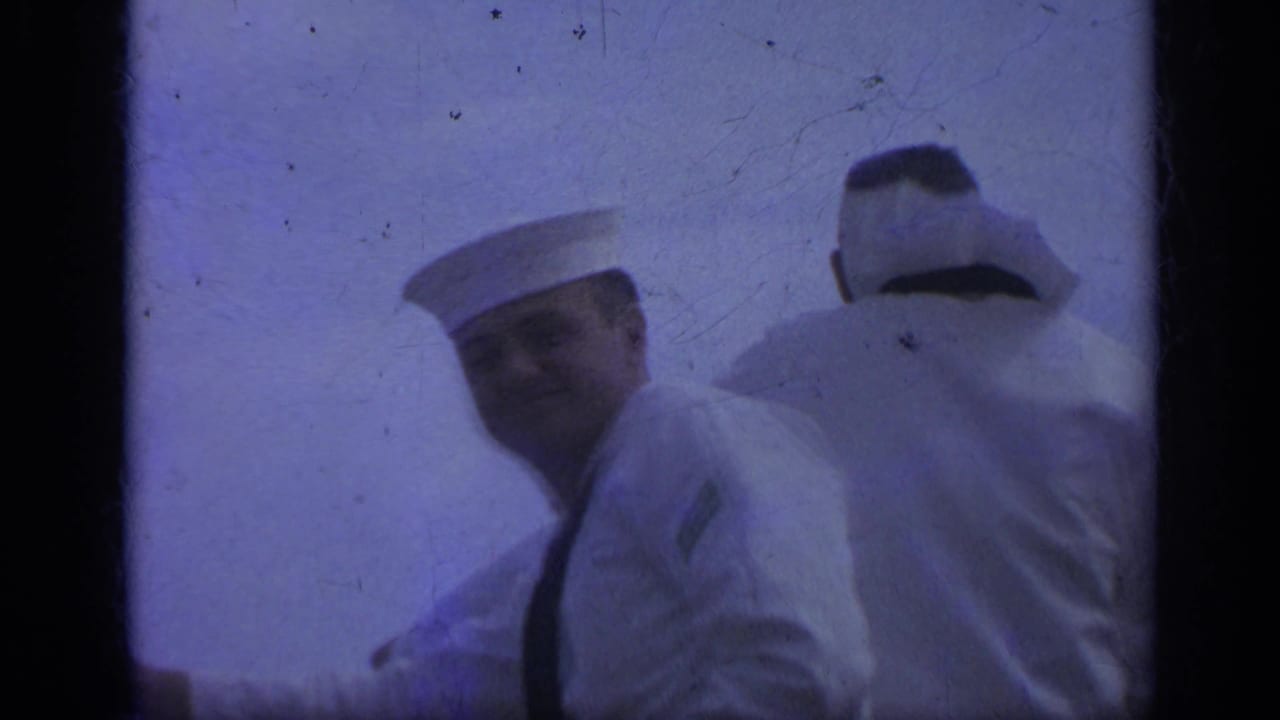 Two sailors in white uniforms on a ship with sea and sky behind them.