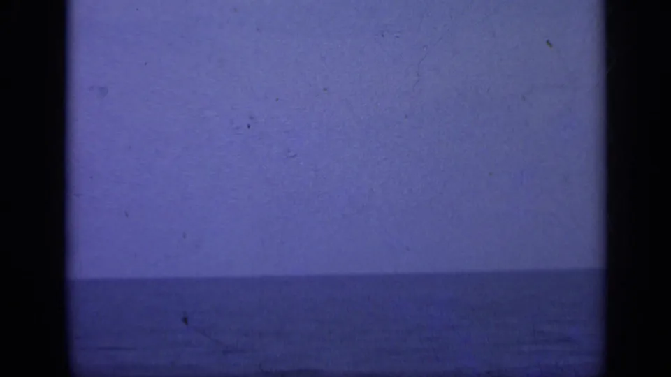 A handheld 8mm view of calm sea and hazy sky follows the sailors, with no people visible in this frame.