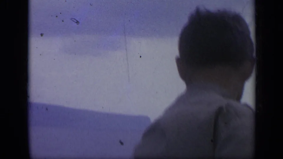 1962 Italian 8mm frame with a silhouetted person seen from behind, facing the sea and distant coastline.