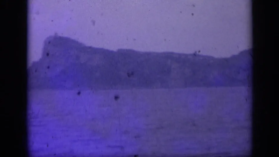 1962 Italian 8mm seascape showing an island shoreline across calm water with strong purple-blue aging.