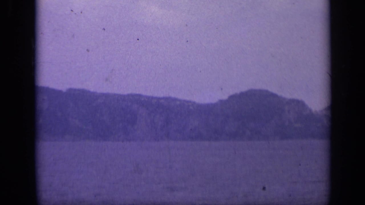 Calm water with a distant rocky shoreline under a hazy sky.