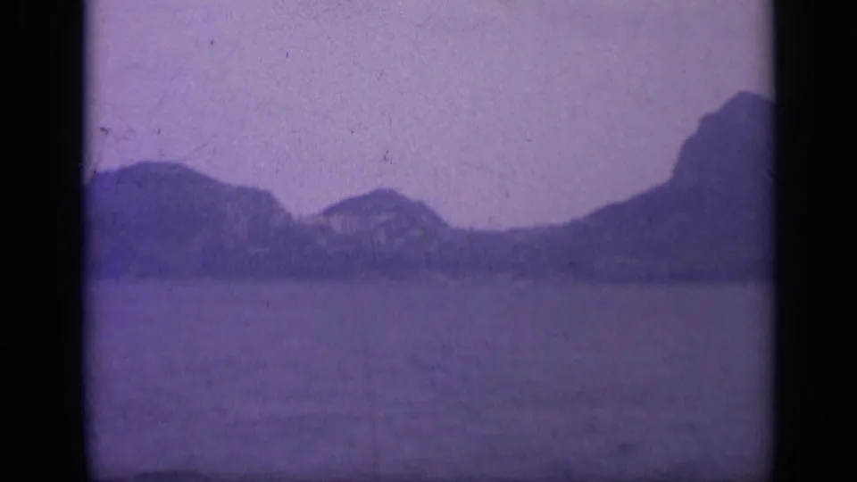 1962 Italian 8mm frame with open water, distant rocky hills, and dark film-frame edges.
