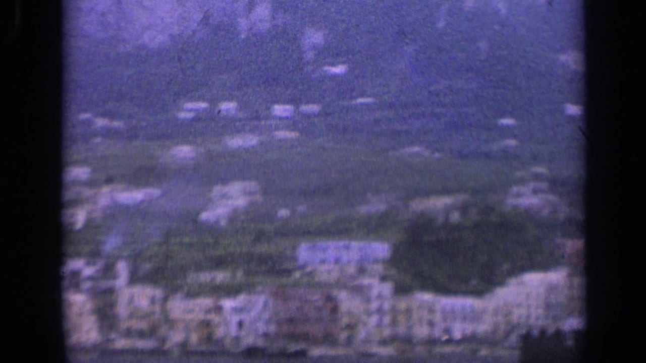 Soft 1962 Italian village view showing clustered hillside buildings, terraces, and a mountain rising behind them.