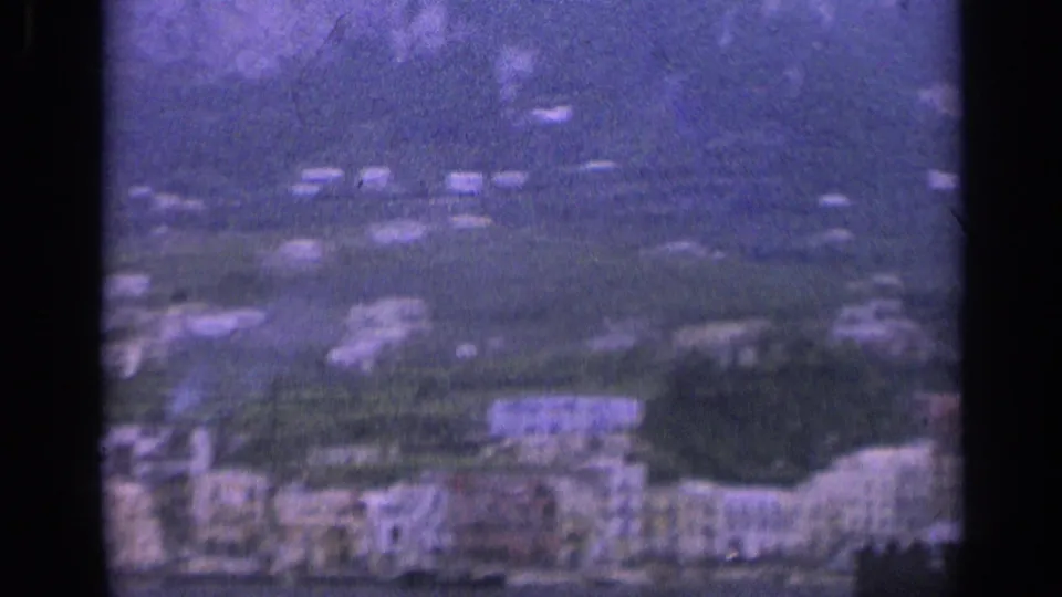 Soft 1962 Italian village view showing clustered hillside buildings, terraces, and a mountain rising behind them.