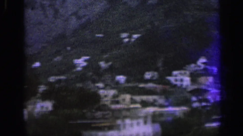 Underexposed 1962 Italian hillside view with scattered homes, dense greenery, and mountain slopes in soft 8mm color.