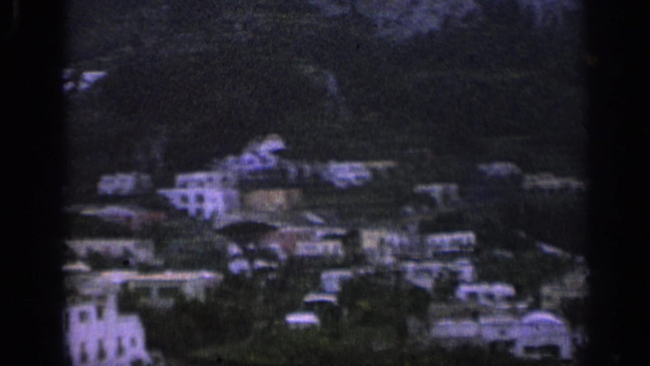 Distant hillside village with pale buildings among green slopes.