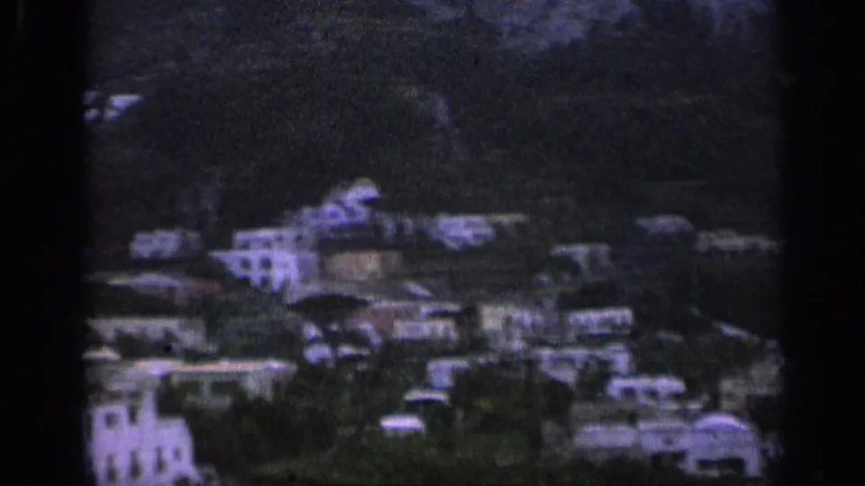 1962 Italy 8mm frame showing pale hillside buildings scattered across green terraced terrain.