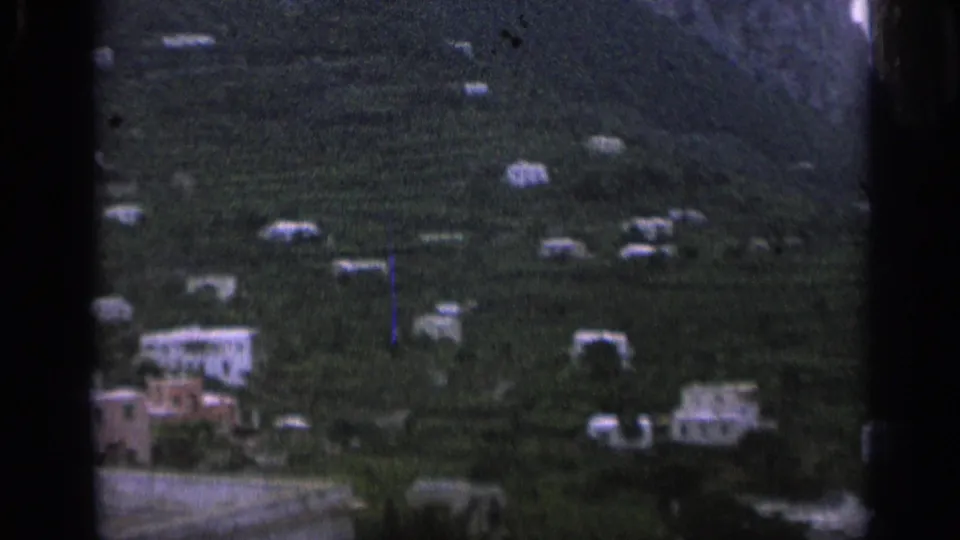 1962 Italy home-movie frame showing scattered pale structures across terraced green slopes.