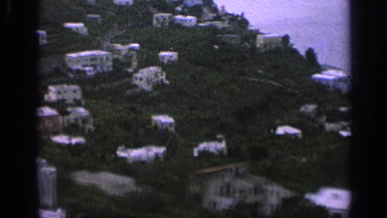 Green hillside with white houses and a partial coastline at the right edge.