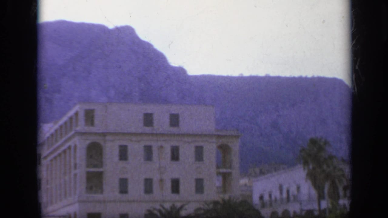 Multi-story building with arched openings below a mountain backdrop.