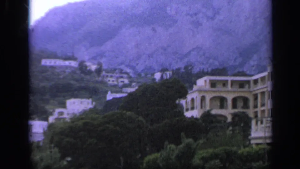 1962 Italy 8mm travel frame showing hillside buildings, dense greenery, palms, and steep mountains.