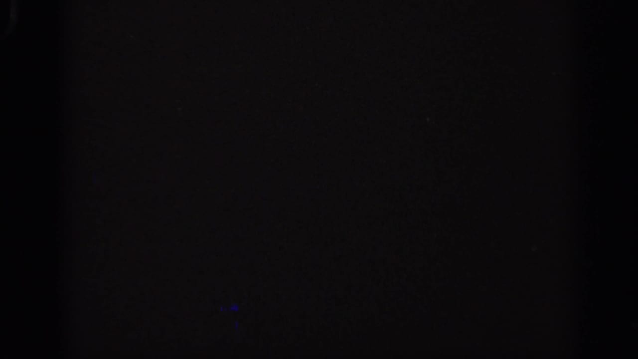 Dark film frame with a central vertical band and faint blue light mark.