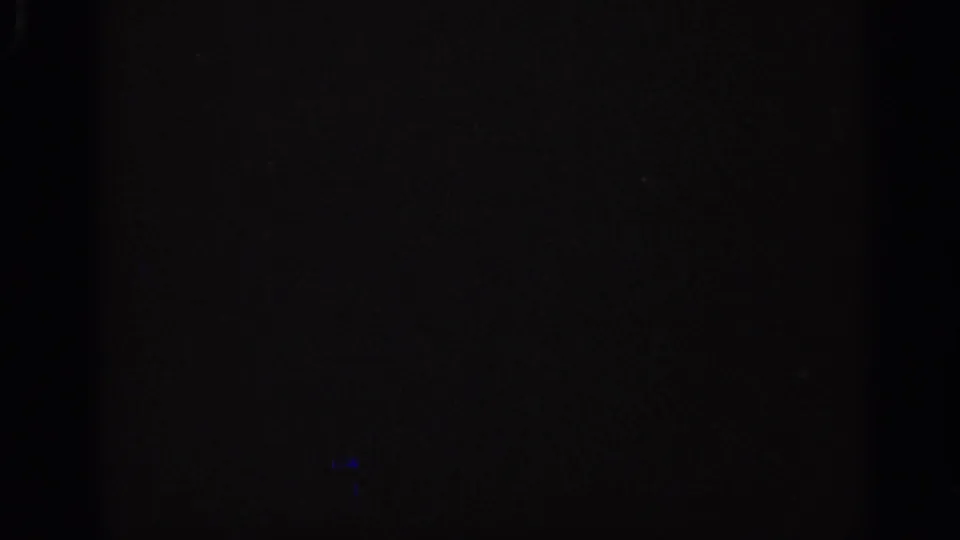 Dark 1962 Italian 8mm frame showing a central vertical band, faint grain, and a small blue flare-like mark.