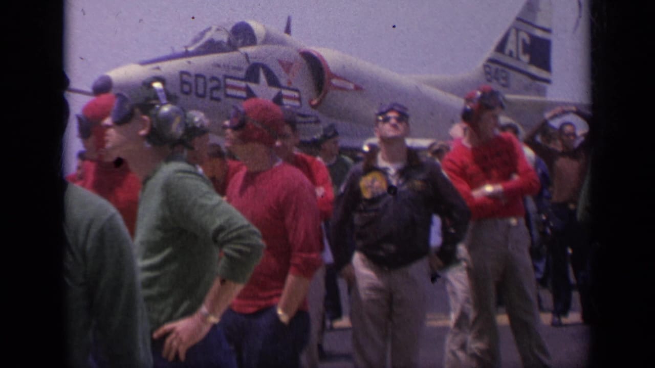 On a 1962 Italy aircraft carrier deck, red-jacketed personnel and others stand near a naval jet with visible markings.